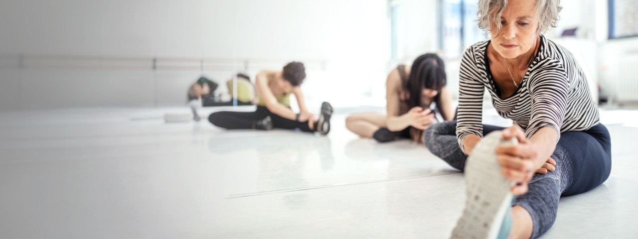 Focused woman stretches leg on floor in workout class. 